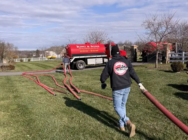 King and Sons technician pulling the suction hose across a customer's lawn with the pump truck in the driveway